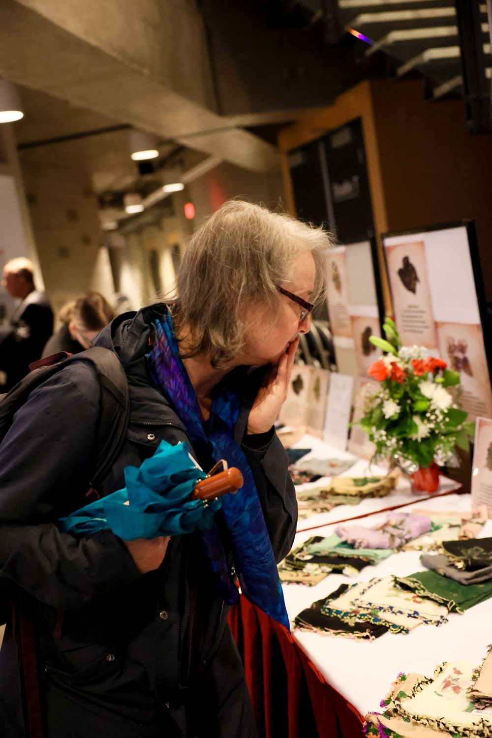 Person examining items on display at what appears to be a convention or exhibition table with flowers and artwork.