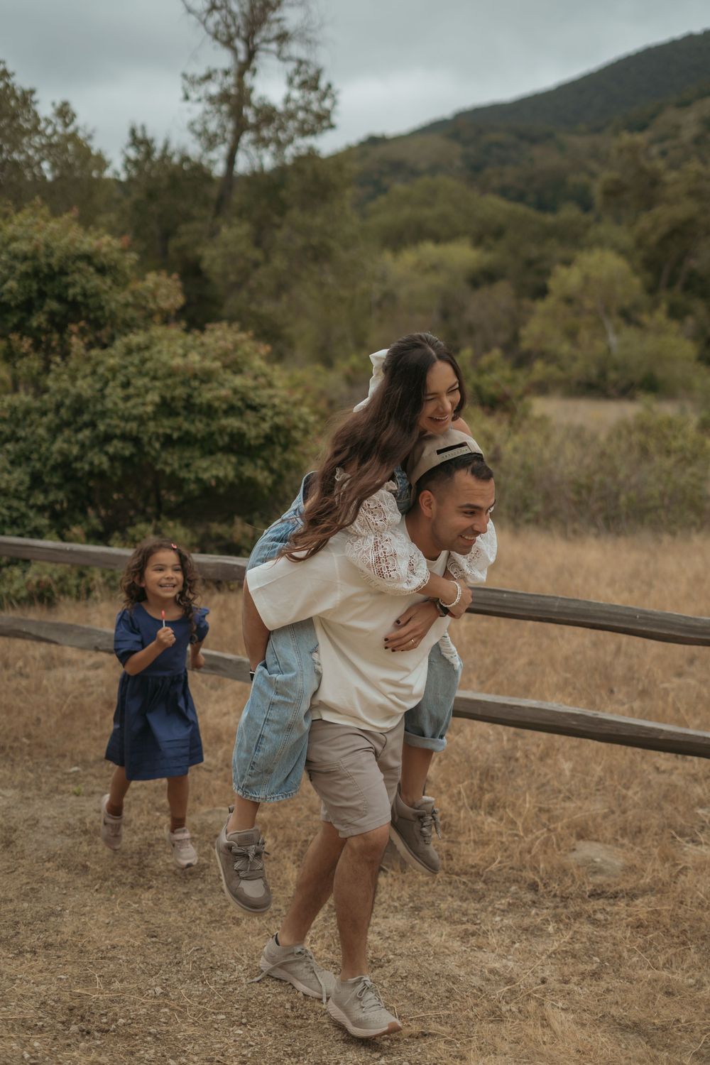 Family enjoying a playful moment on a mountain trail surrounded by autumn foliage and natural scenery.