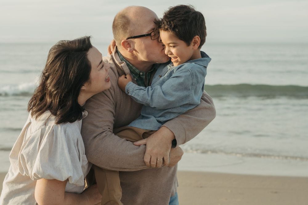 A family shares a tender moment together while standing on a misty beach at sunset.