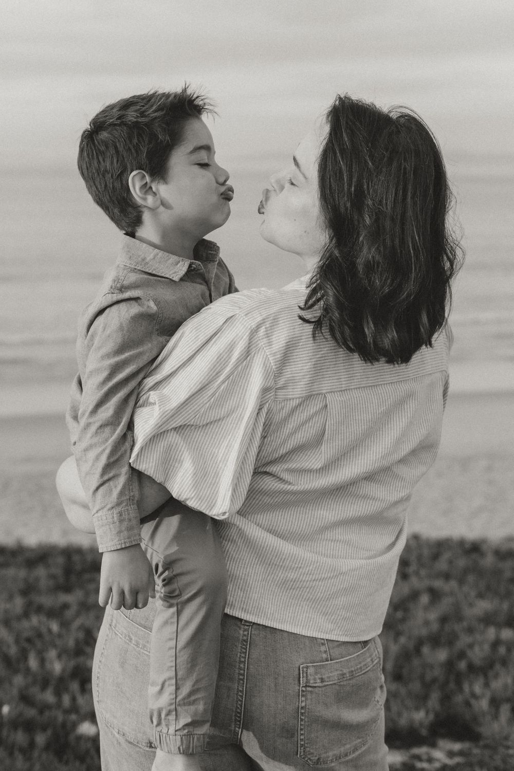 Black and white photo series showing a playful moment between two people in jeans and white shirts on a grassy hill.