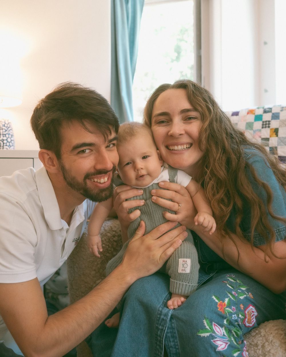 A smiling couple holds their happy baby in a cozy living room, capturing a joyful family moment together.