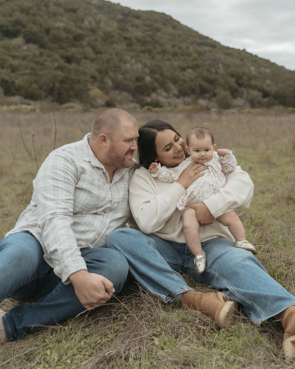 A family lying together on a grassy hillside in casual clothing enjoying a tender outdoor moment together.
