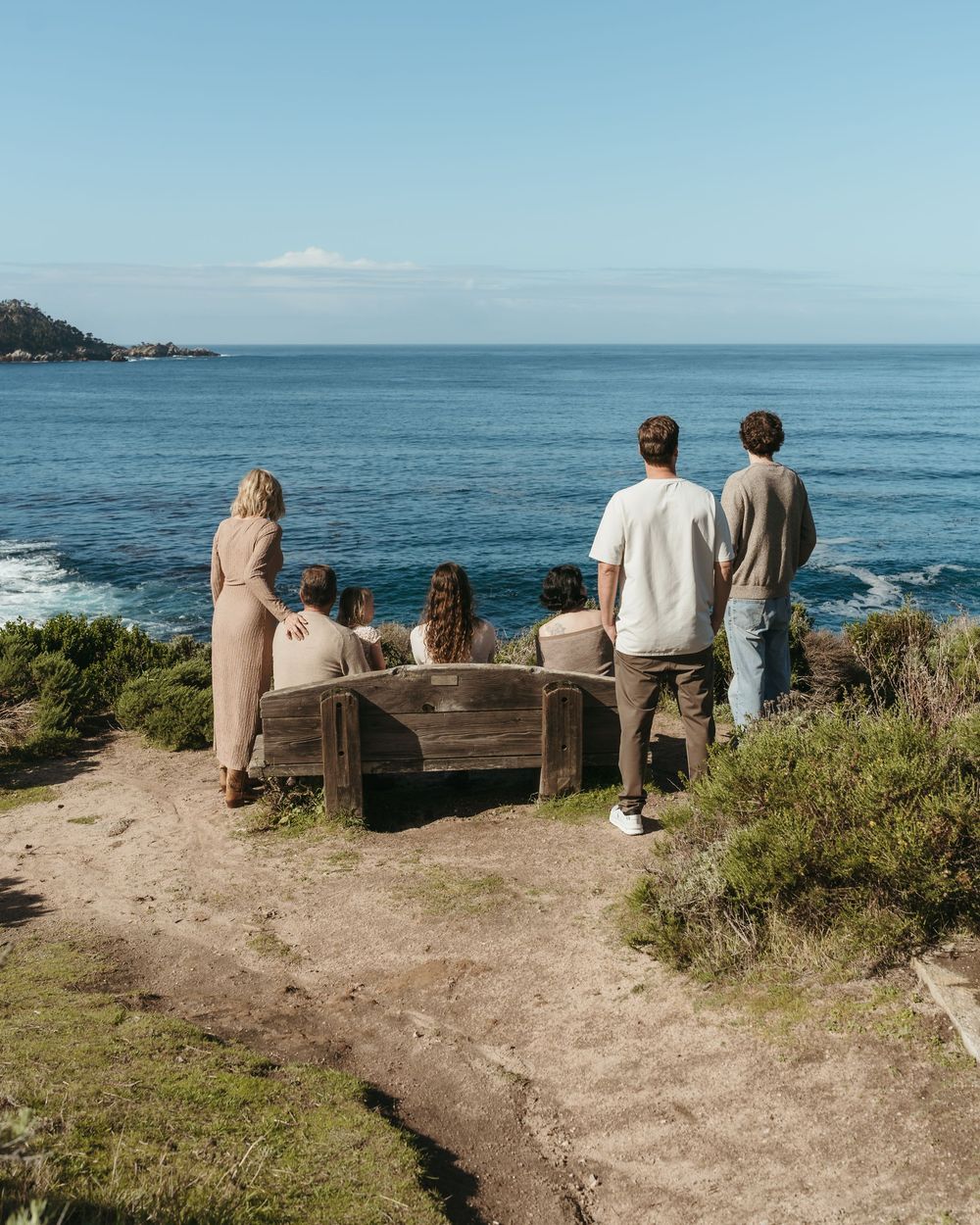 A group of visitors admire the scenic Pacific Ocean view from a coastal overlook on a sunny day.