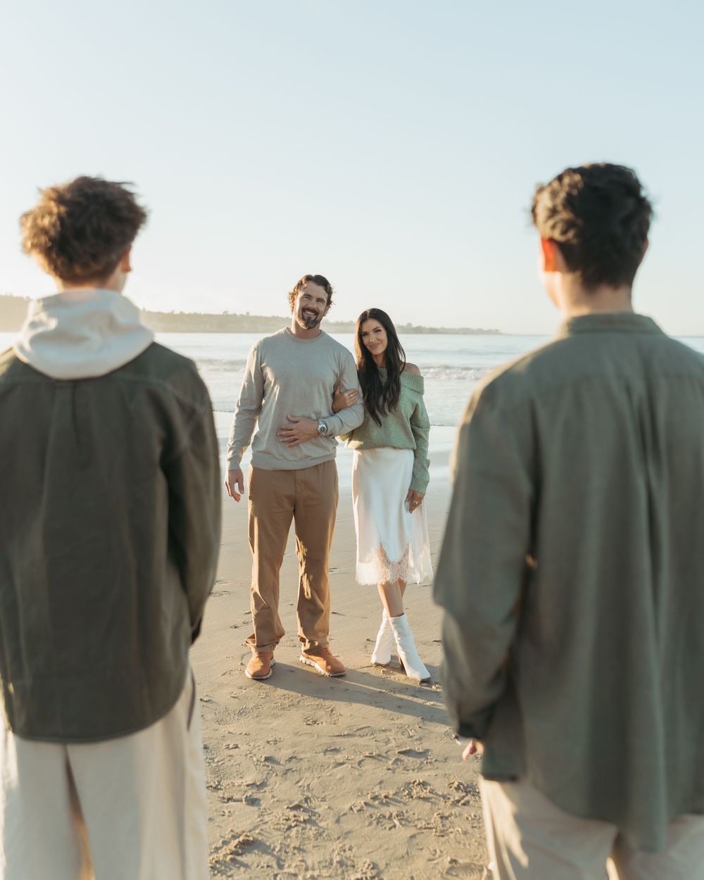 Group walking together on a sunny beach with casual attire and warm lighting at sunset.