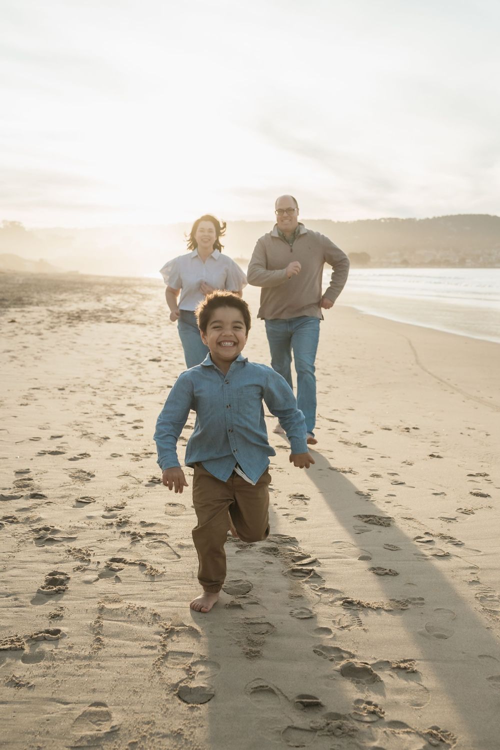 Family enjoying a sunset beach walk while a child runs playfully ahead on the sand.