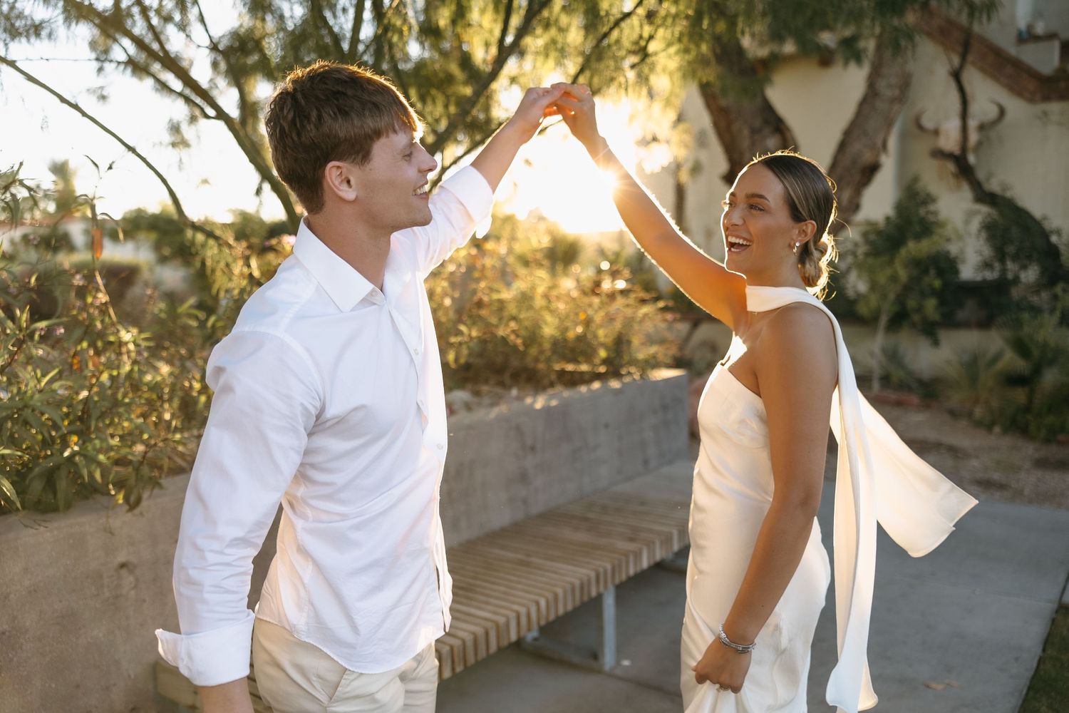 Couple in white formal wear dancing outdoors during golden hour.