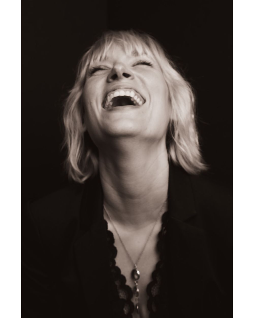 Black and white portrait capturing joyful laughter with head tilted back.