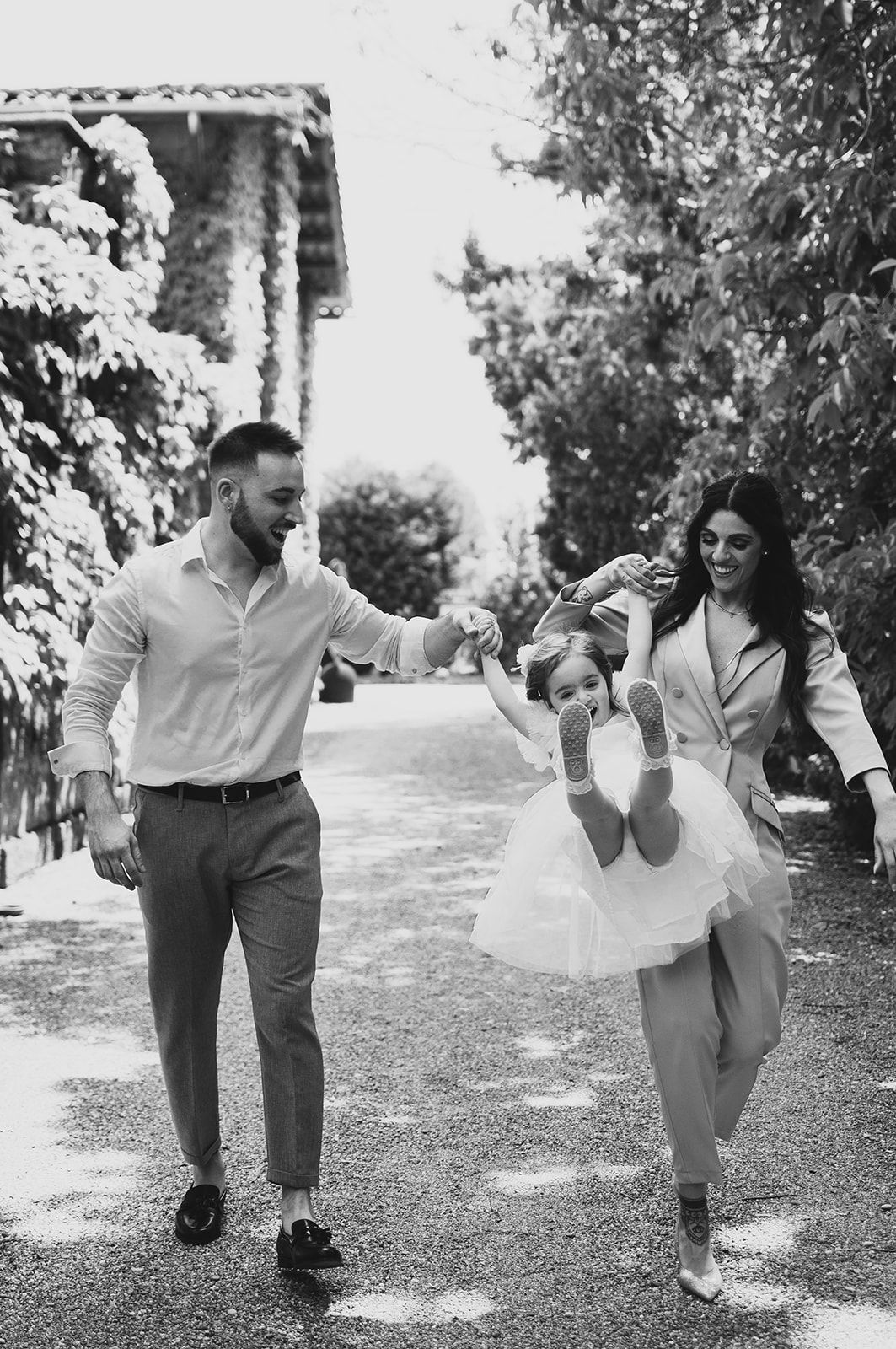 Giocosa sequenza in bianco e nero di una famiglia che corre e balla su un sentiero del giardino in provincia di Alessandria, battesimo.