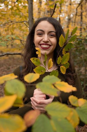 À Liège, au bois du Sart-Tilman, portrait de femme photographiée en extérieur en automne, riant et tenant une branche de feuilles