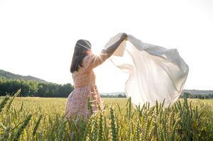 Femme photographiée à Andenne au coucher de soleil dans un champ de blé en été tenant un drap blanc