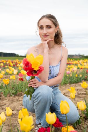 À Huy, portrait de femme photographiée en extérieur,  accroupie dans un champs de tulipes avec un bouquet de fleurs dans la main