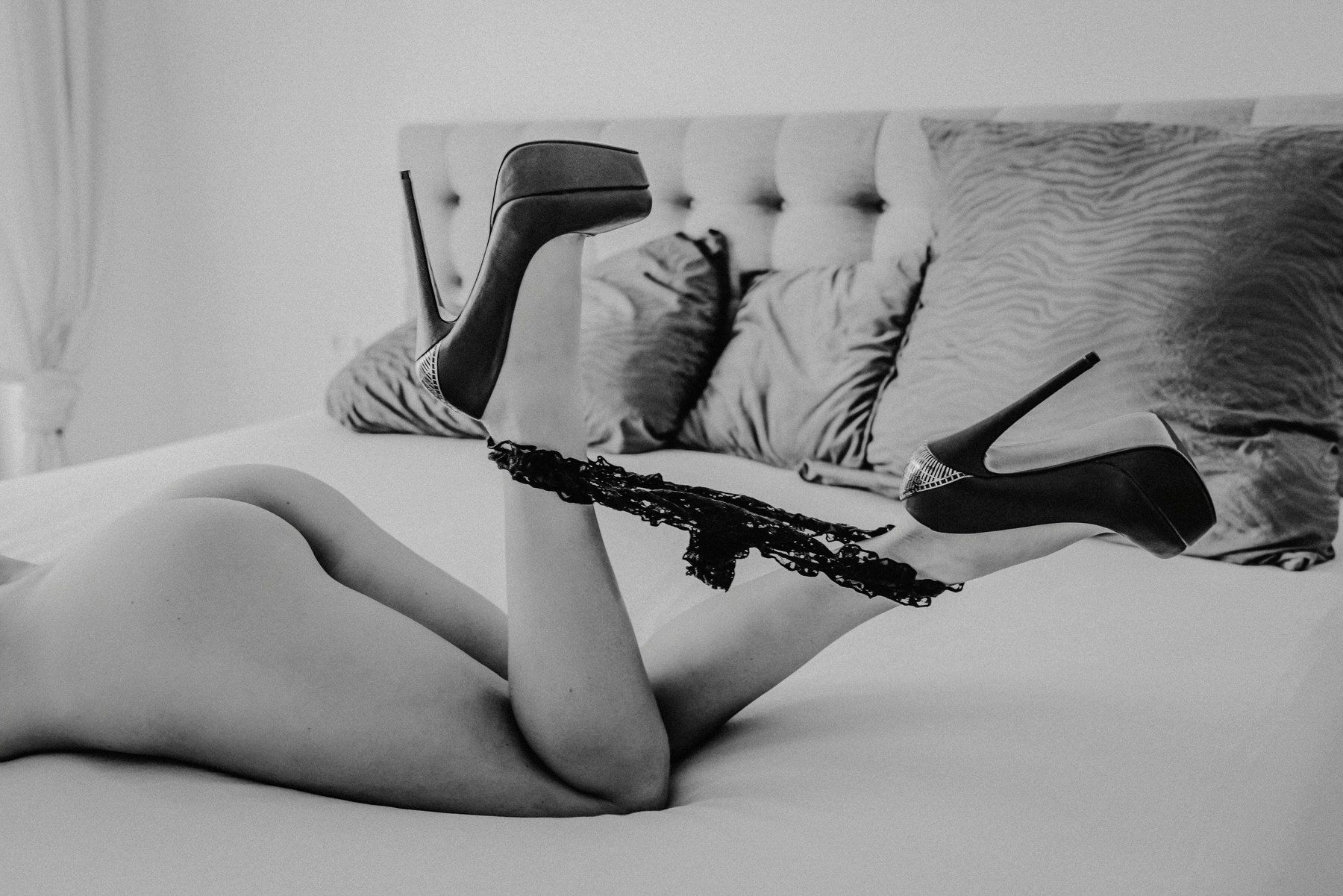 High-heeled boots shown on a bed with soft cushions in black and white photography.