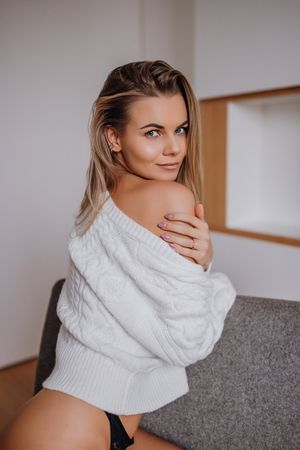 Sensual portrait of someone in a cozy white sweater posing seductively on a grey couch.