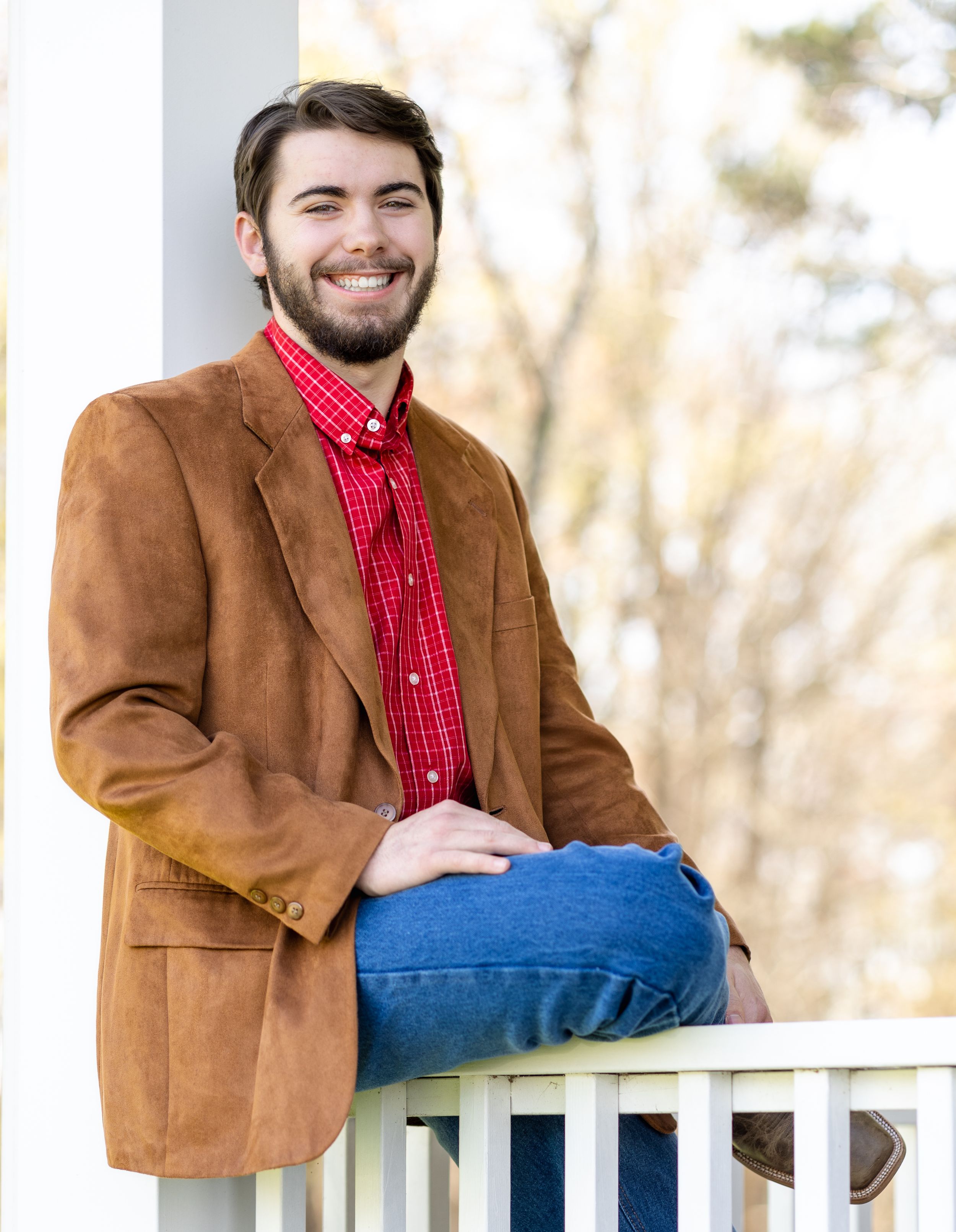 Casual portrait in brown corduroy blazer and red plaid shirt on white porch railing.