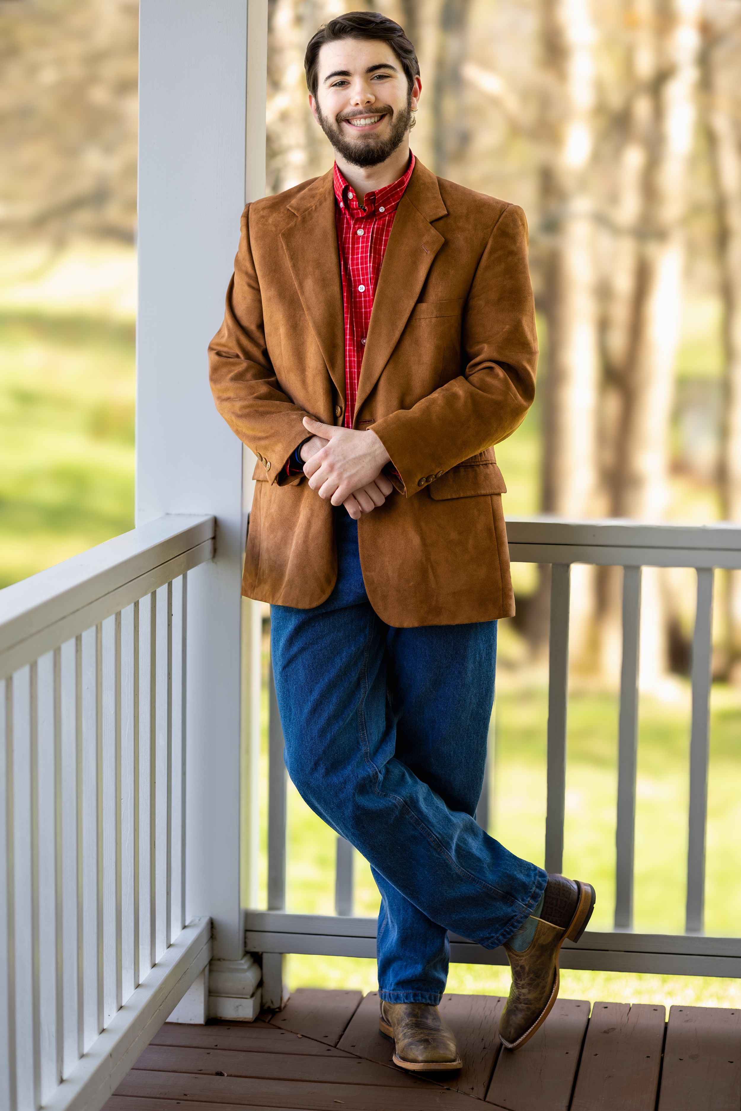 Stylish pose in brown blazer and jeans leaning against white porch railing.