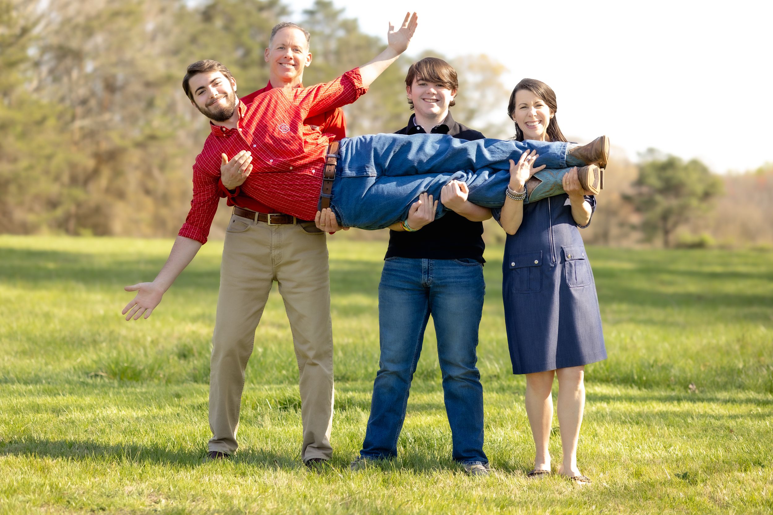 Cheerful group strikes fun poses together on grassy hill during outdoor photoshoot.