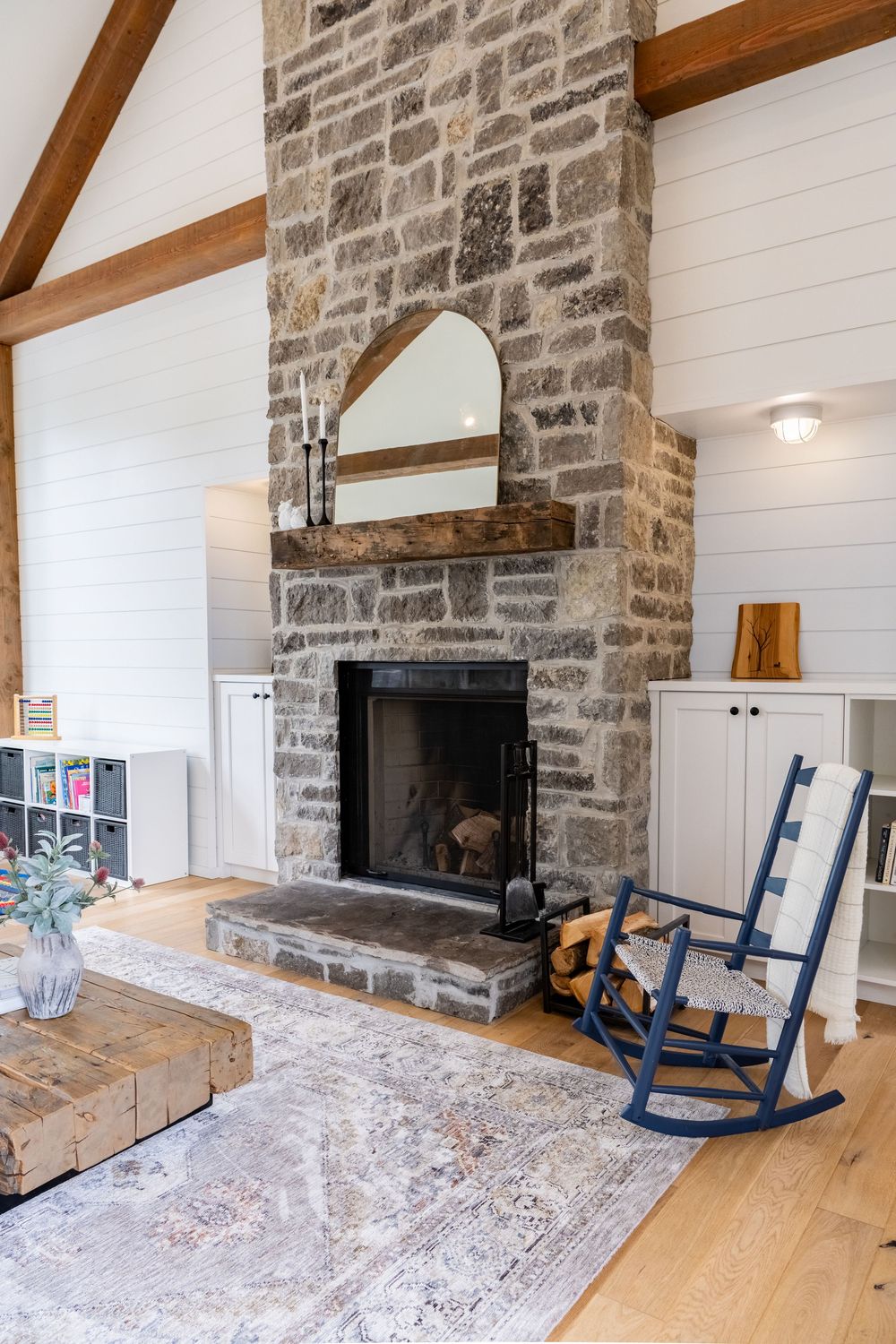 Rustic living room with stone fireplace, wooden beams, and navy rocking chairs.