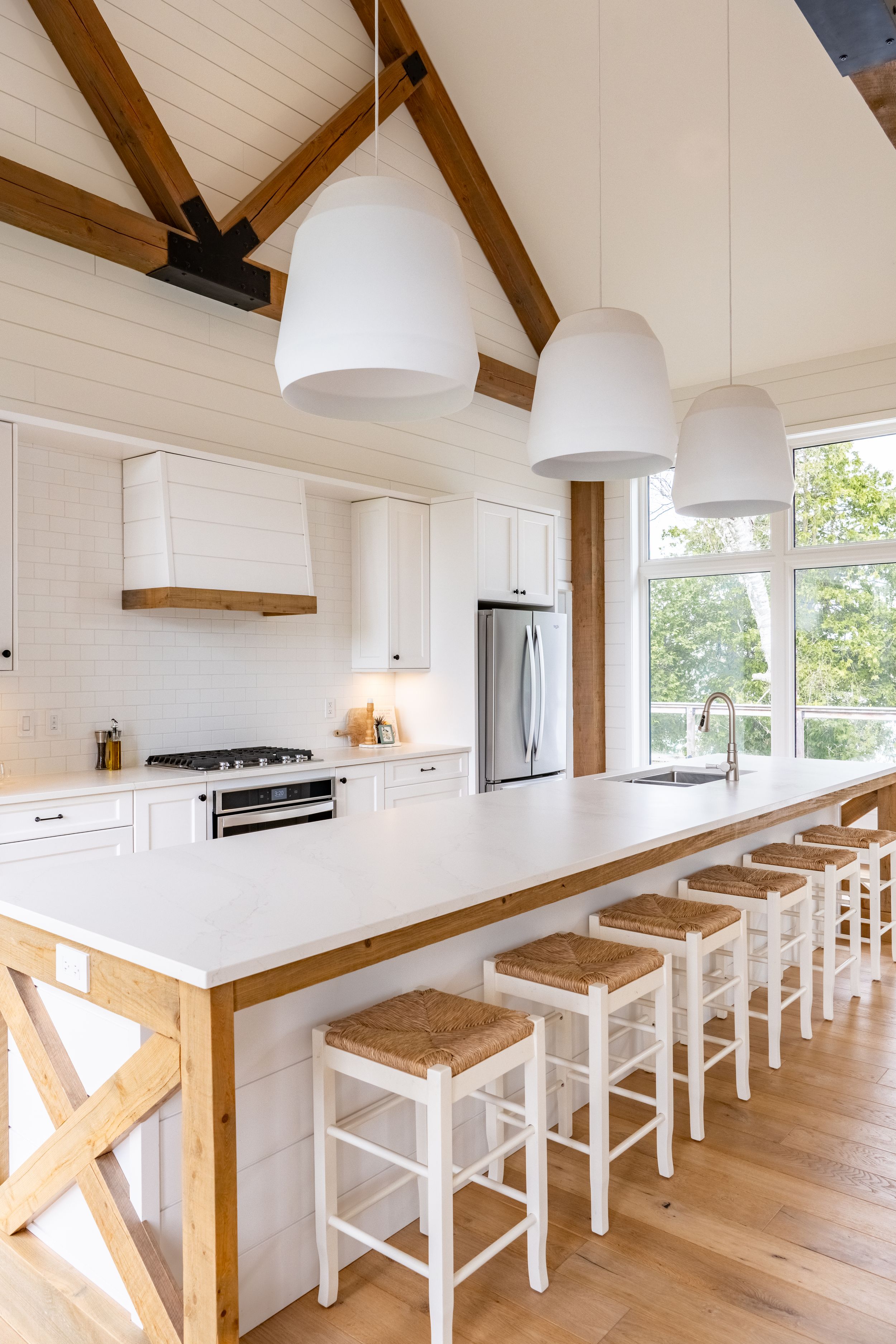 Modern white kitchen with vaulted ceiling, wooden beams and bar seating.