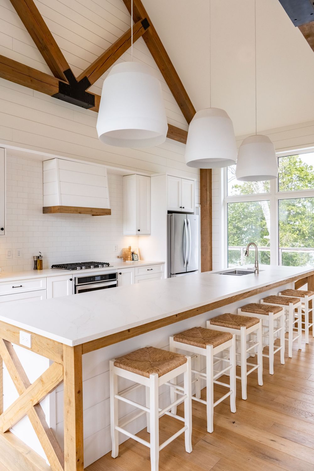 Modern white kitchen with vaulted ceiling, wooden beams and bar seating.
