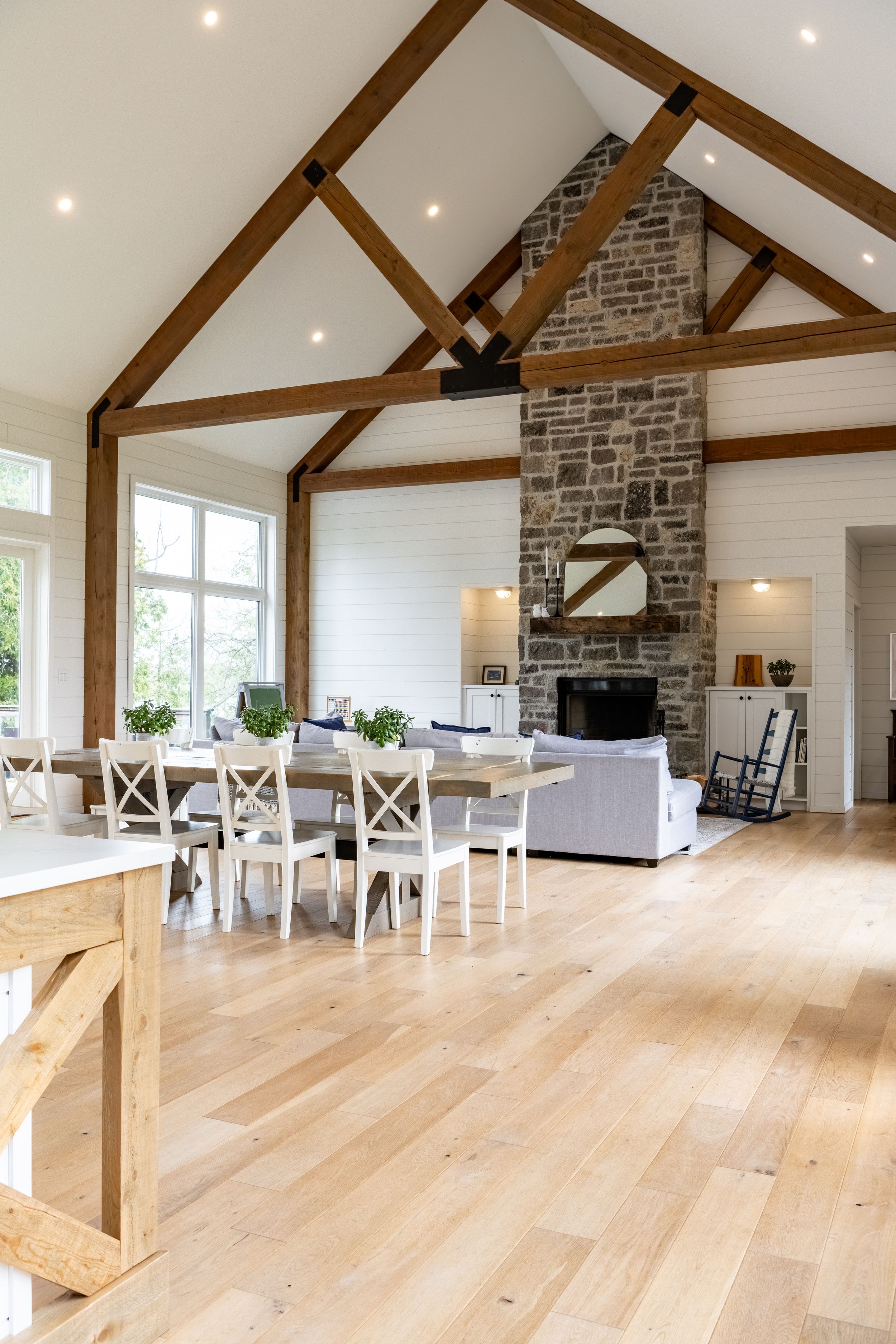 Open concept living space with exposed beams, light wood floors and stone fireplace.