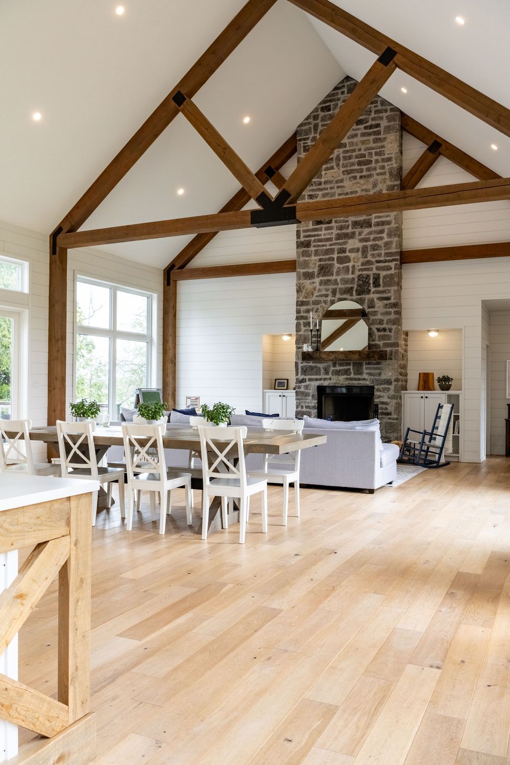 Open concept living space with exposed beams, light wood floors and stone fireplace.