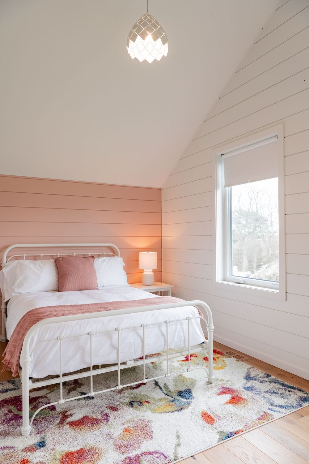 Airy bedroom with shiplap walls, floral rug and white metal bed frame.