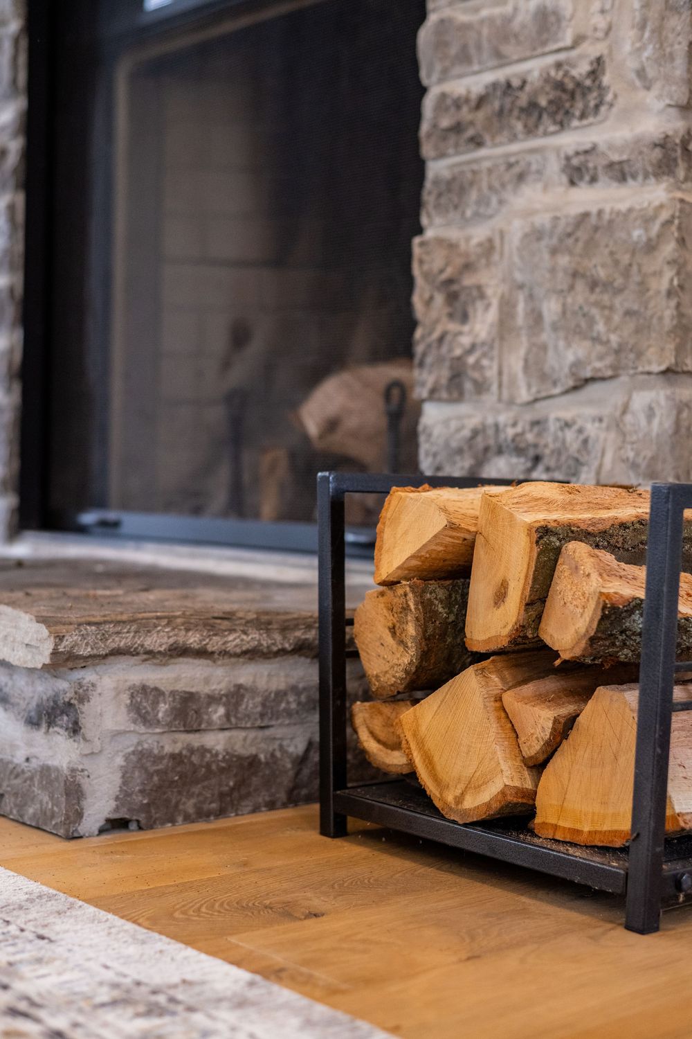 Stacked firewood in a metal holder next to a stone fireplace.