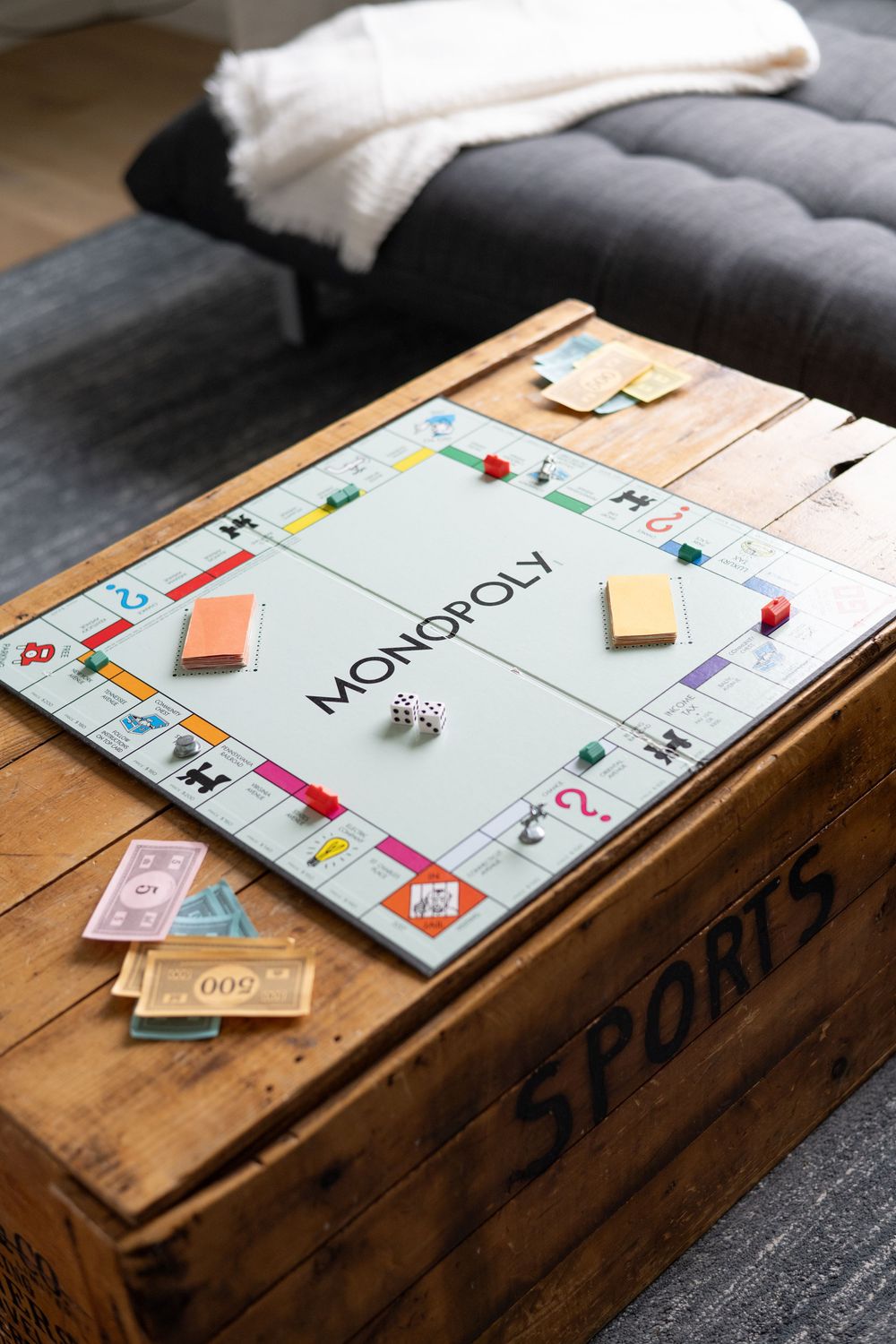 Monopoly board game set up on a wooden trunk with game pieces and money.