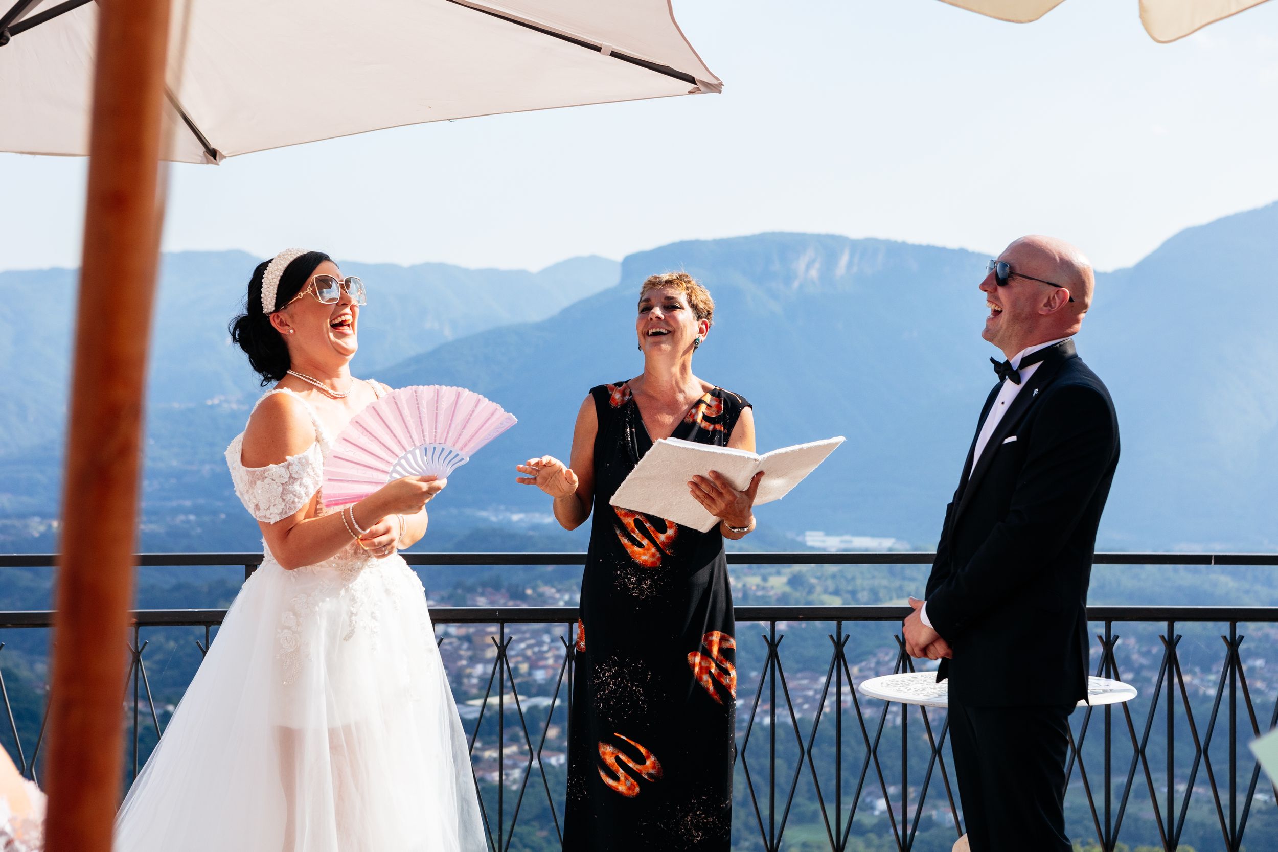 An outdoor wedding ceremony takes place on a terrace overlooking scenic mountain views in warm sunlight near Barga in Tuscany.