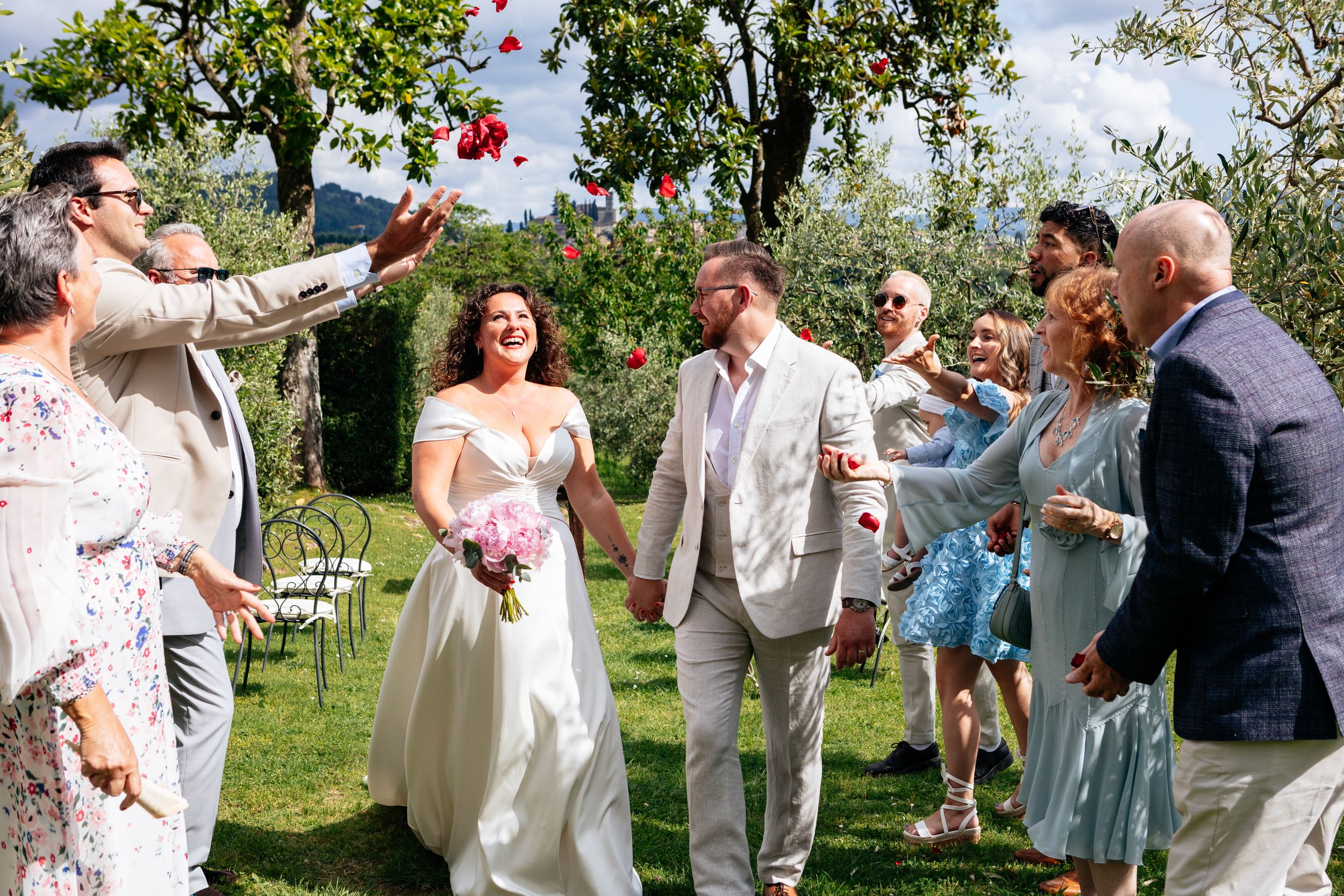 Wedding guests toss red flower petals during an outdoor garden ceremony celebration in Barga, Tuscany.