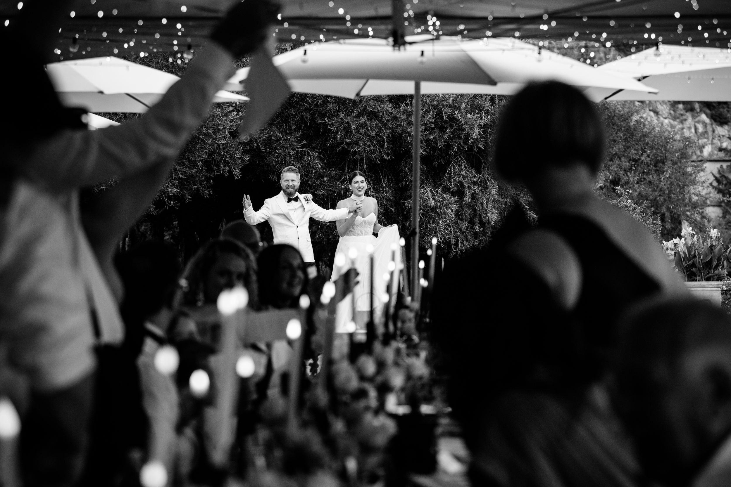 A black and white wedding celebration scene with guests under white umbrellas welcoming the newly weds in Lucca Tuscany.