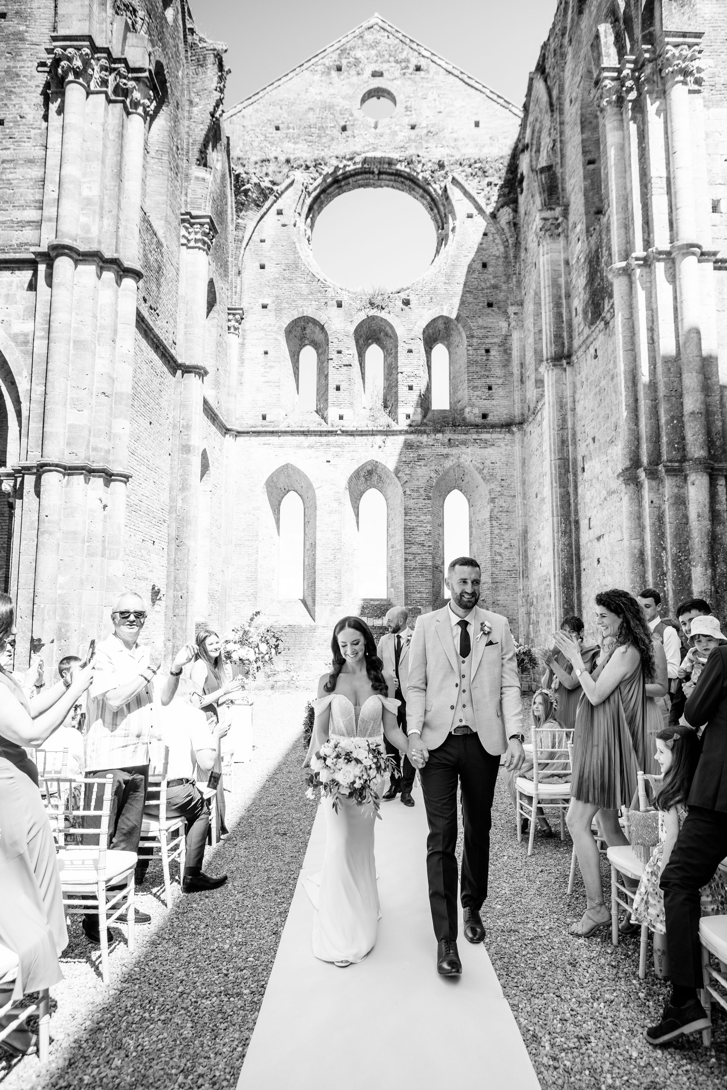 A wedding ceremony takes place in the stunning ruins of the ancient abbey with soaring Gothic arches and stone walls in San Galgano.