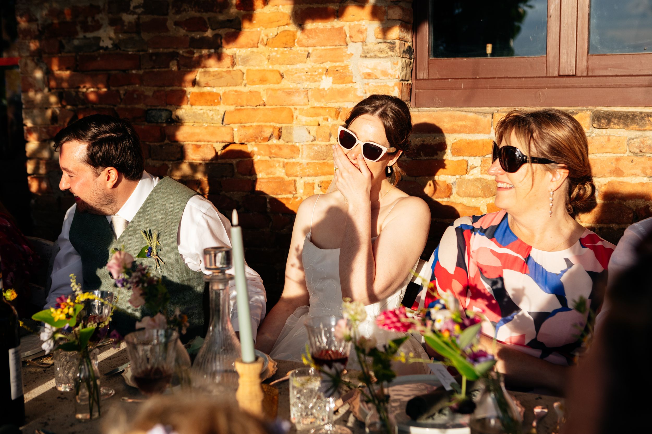 Wedding guests enjoy an outdoor reception with colorful flowers and drinks at a rustic brick venue in warm sunlight at the Lazy Olive.