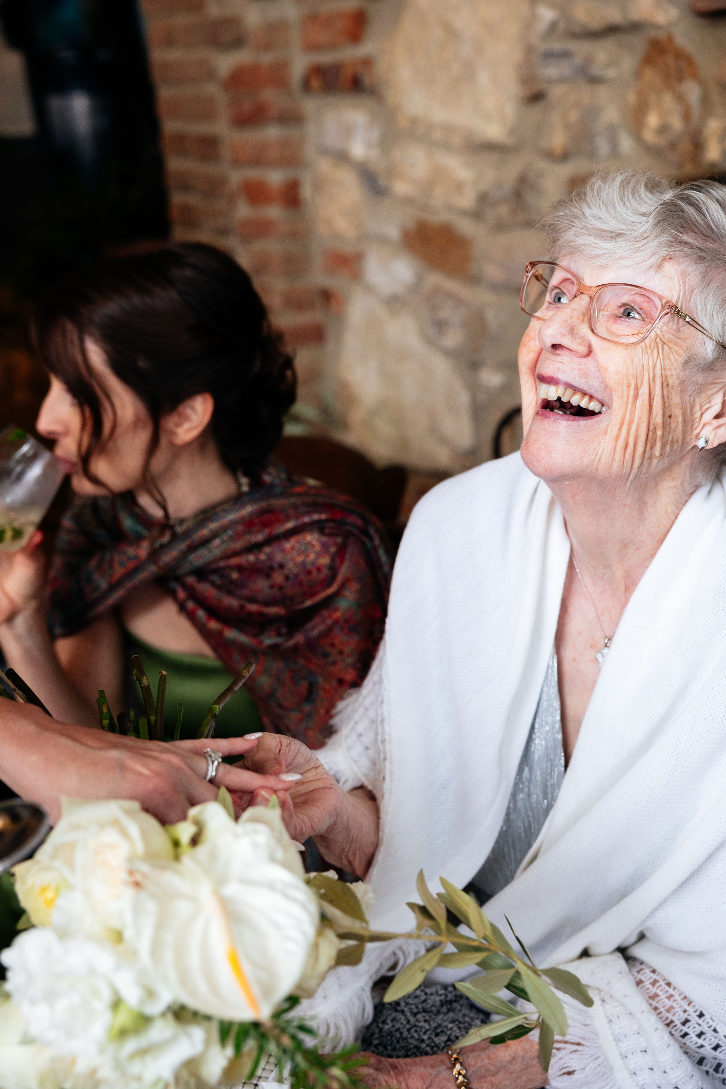 The grandmother of the bride laughs joyfully as she admires the bride's new wedding ring.