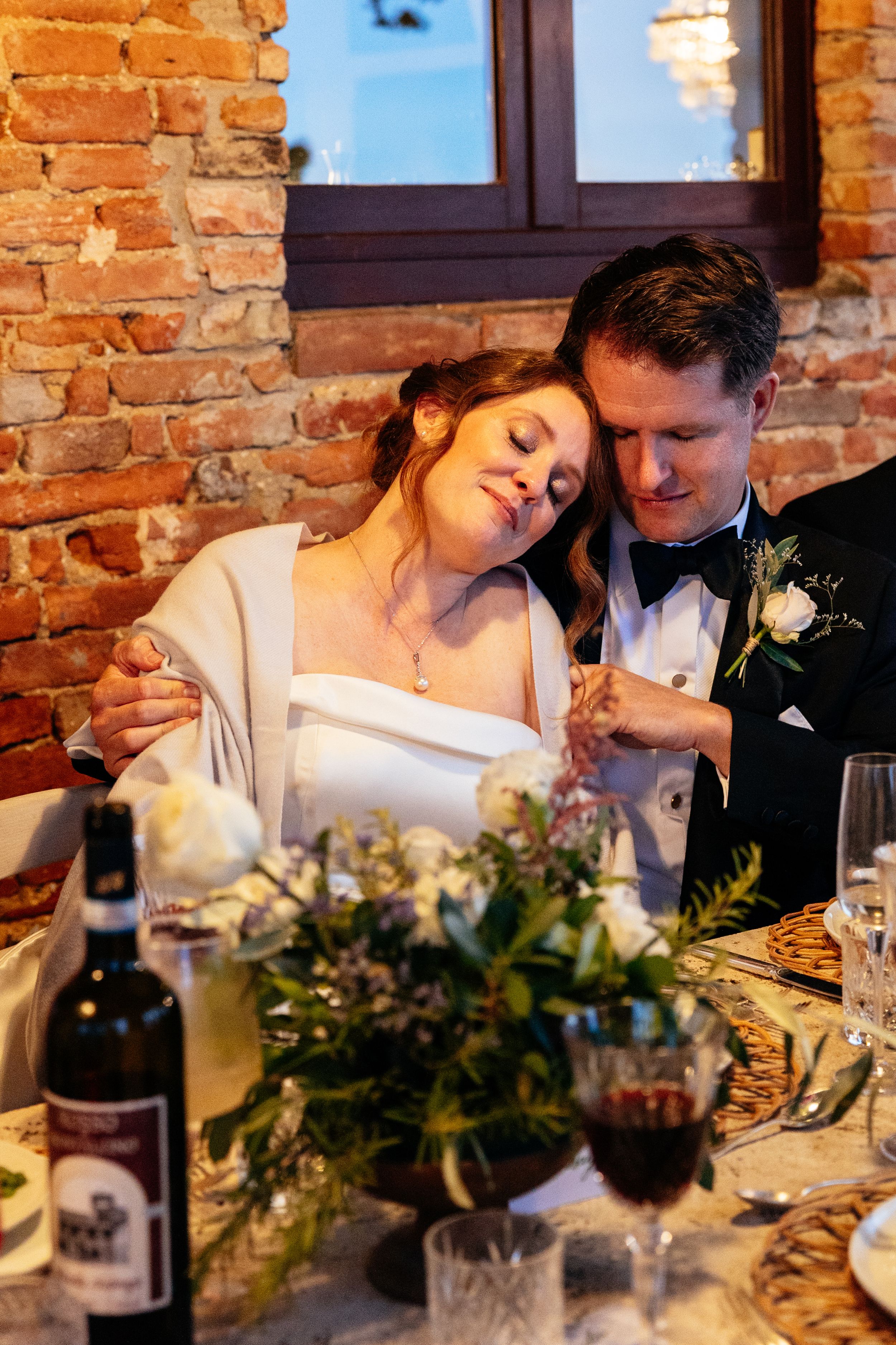 A romantic wedding reception moment at a rustic brick venue with wine and floral centerpieces on the dining table.