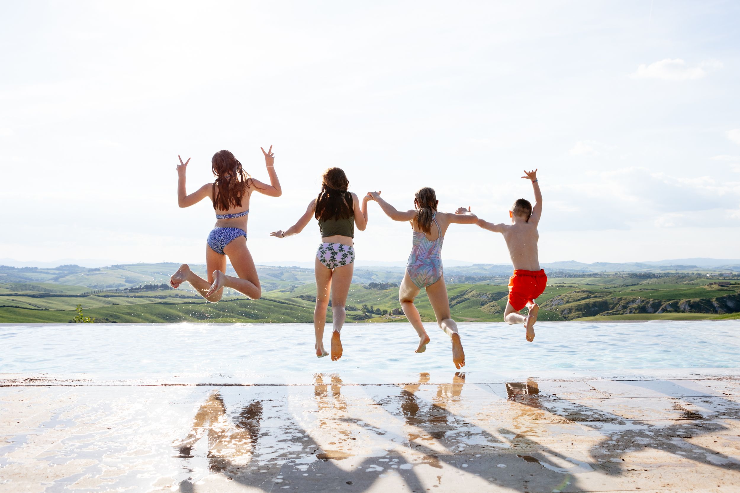 Cousins at a wedding jumping joyfully into the infinity pool at the Lazy Olive in Tuscany.