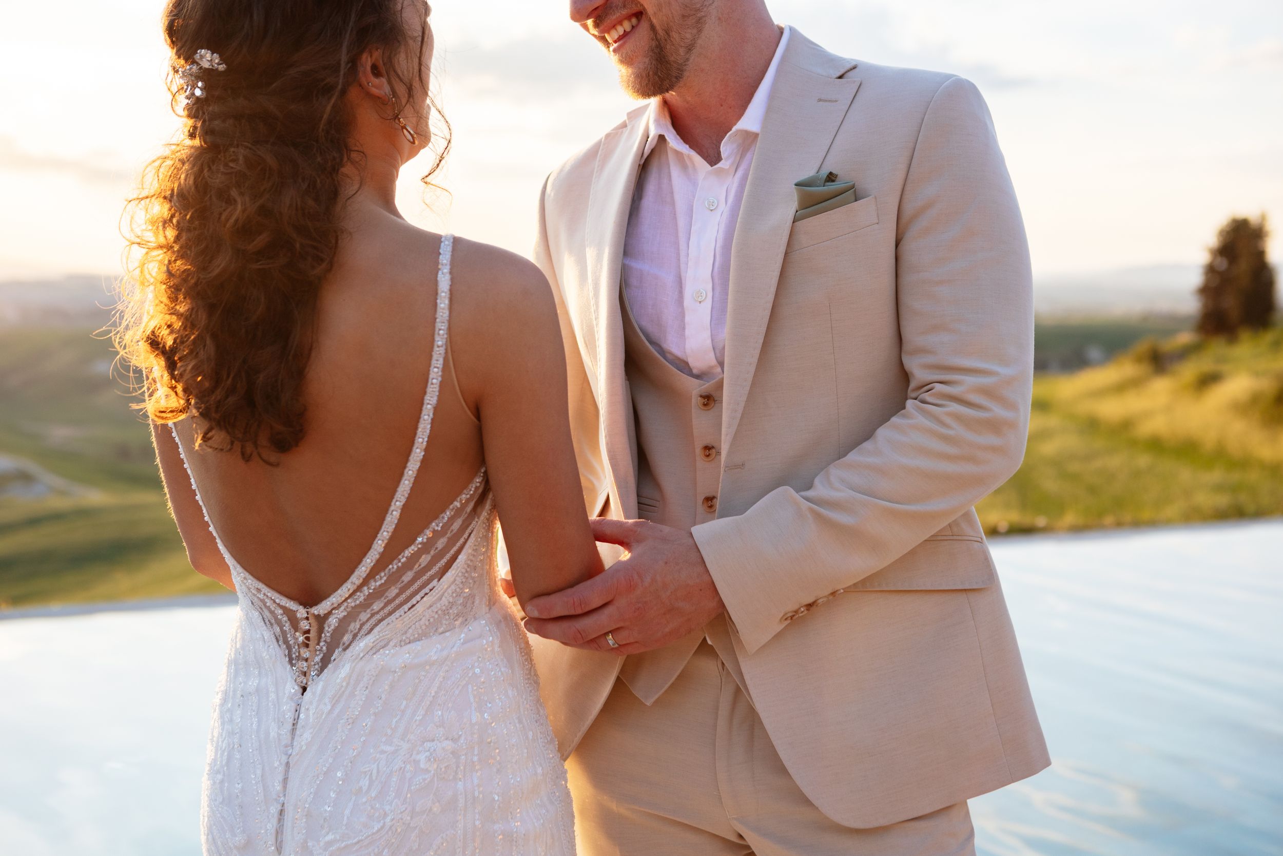 A couple shares an intimate moment at sunset in formal wear on a scenic hilltop.