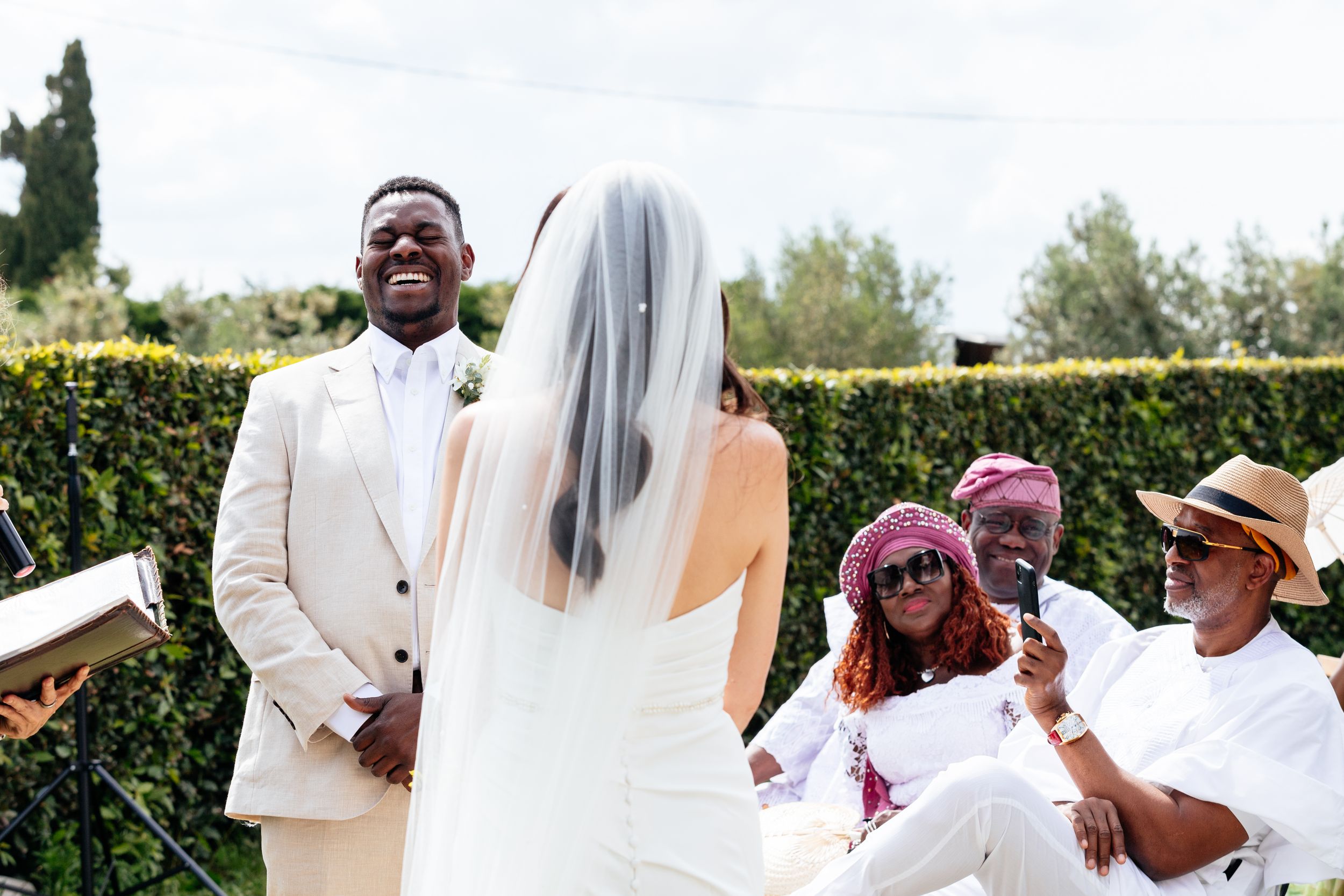 A joyful wedding ceremony takes place outdoors with guests laughing during the vows at Villa Ulignano in Tuscany.