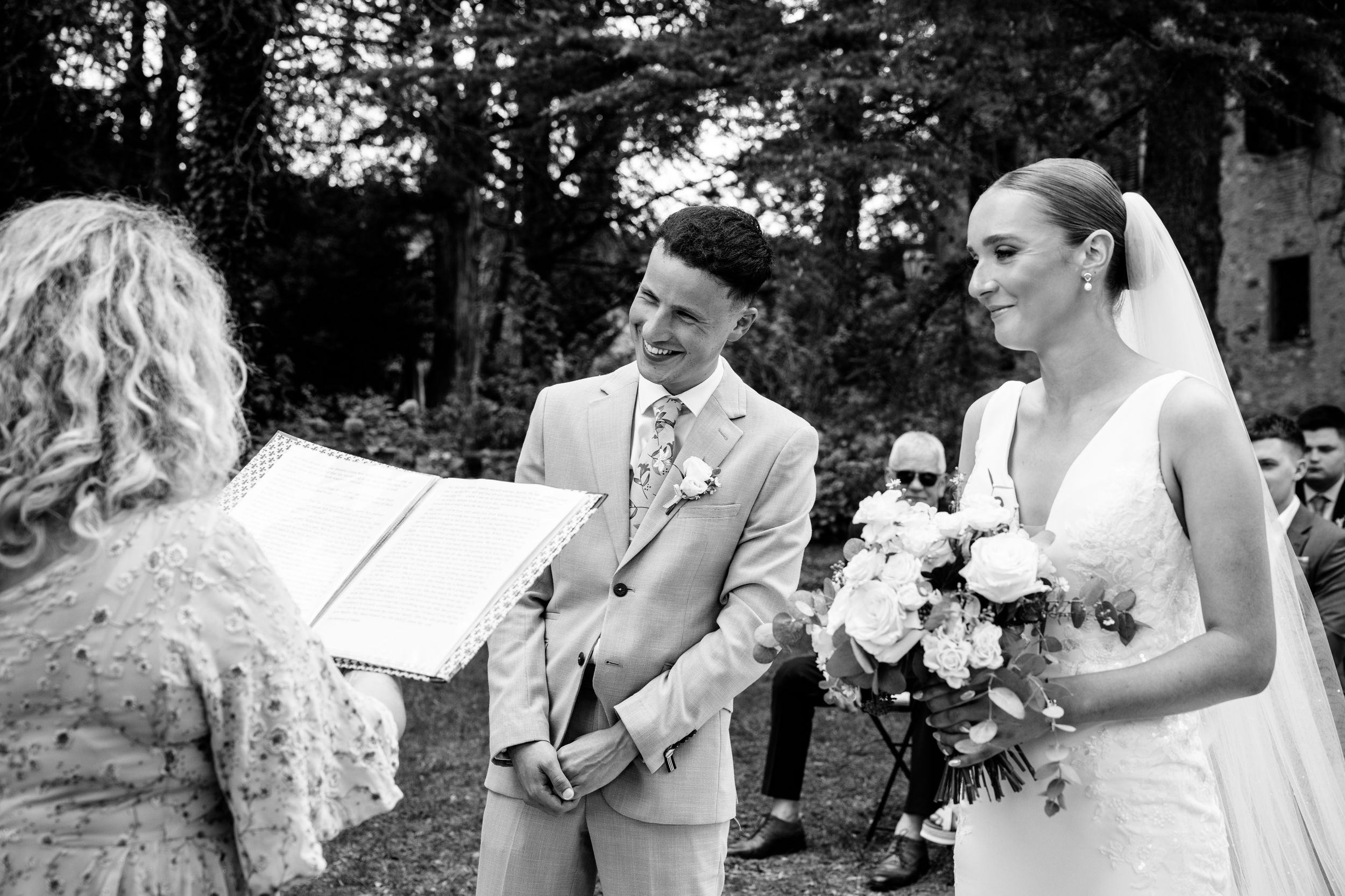 Black and white photo of an outdoor wedding ceremony at Villa Cini with couple and officiant exchanging vows among trees.