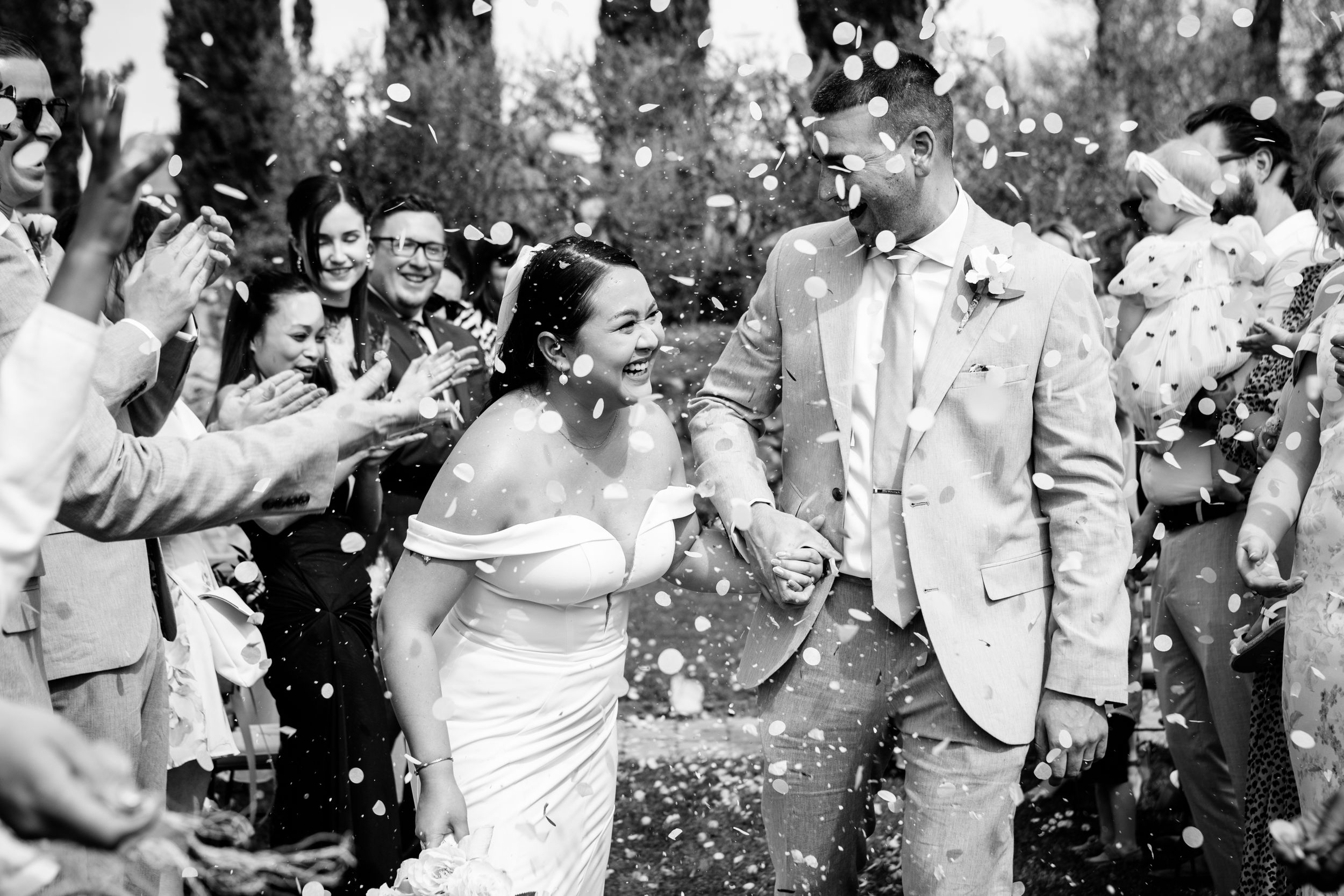 A celebratory wedding scene in black and white with flower petals being thrown by guests as the couple exits at Villa Petrea in Tuscany.