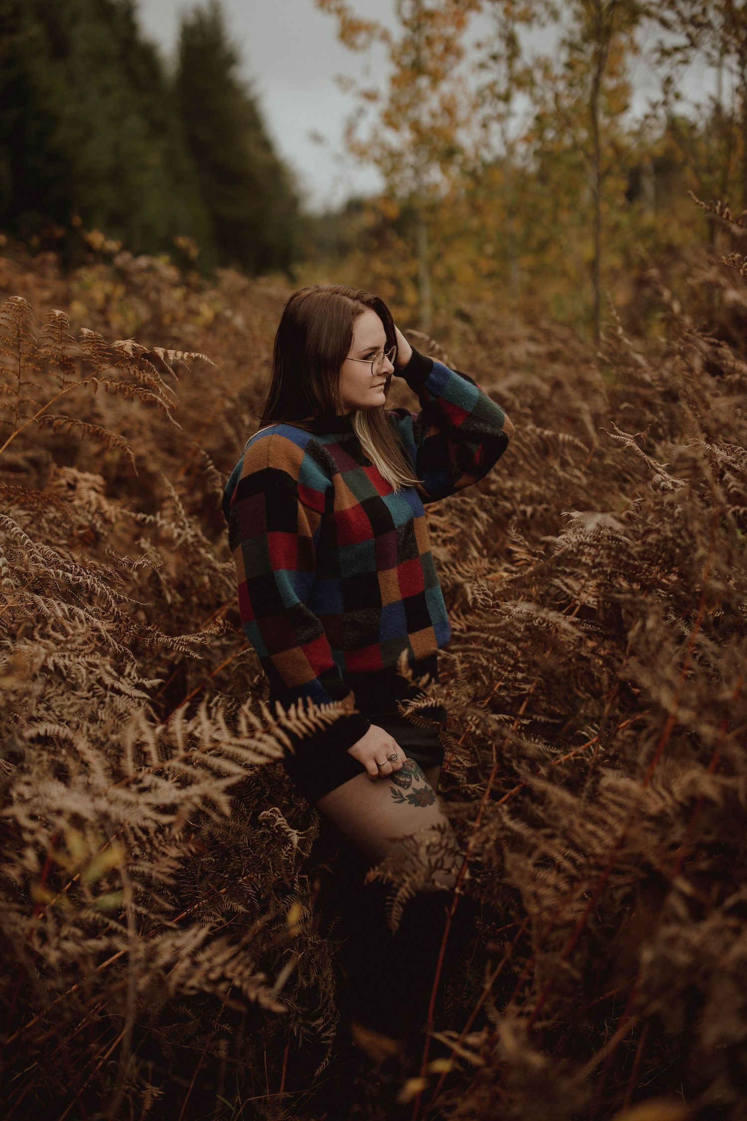 Moody autumn portrait in colorful sweater among ferns and fallen leaves.
