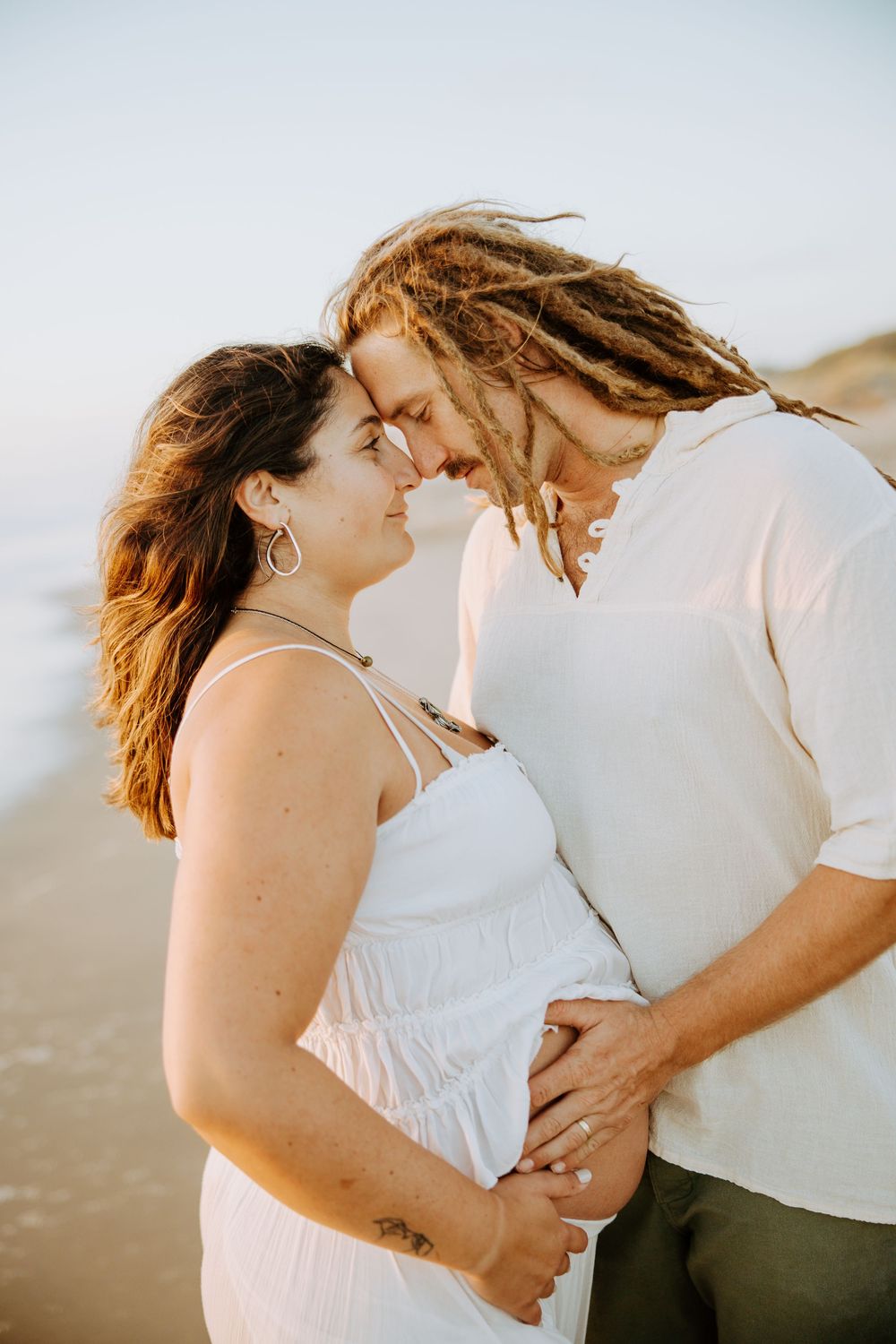 Romantic couple in white outfits embracing tenderly at sunset in a series of intimate beach photos.
