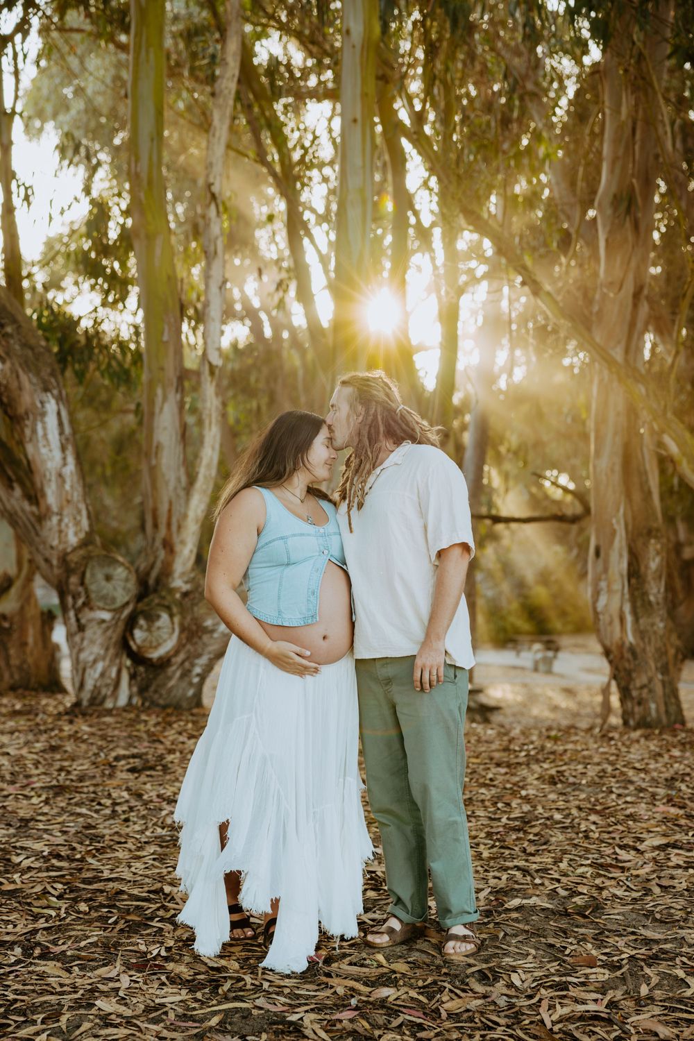 A couple shares an intimate moment among eucalyptus trees at sunset in a natural outdoor setting.