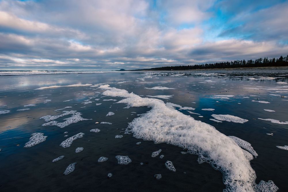 Aerial view of a frozen lake with cracked ice patterns and cloudy skies reflecting on the glassy surface.