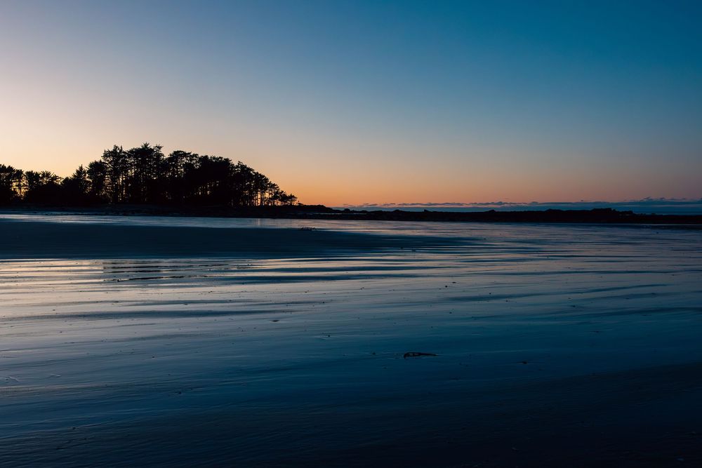 Tranquil sunset view of a silhouetted coastline with calm waters reflecting the dusk sky at a peaceful beach.