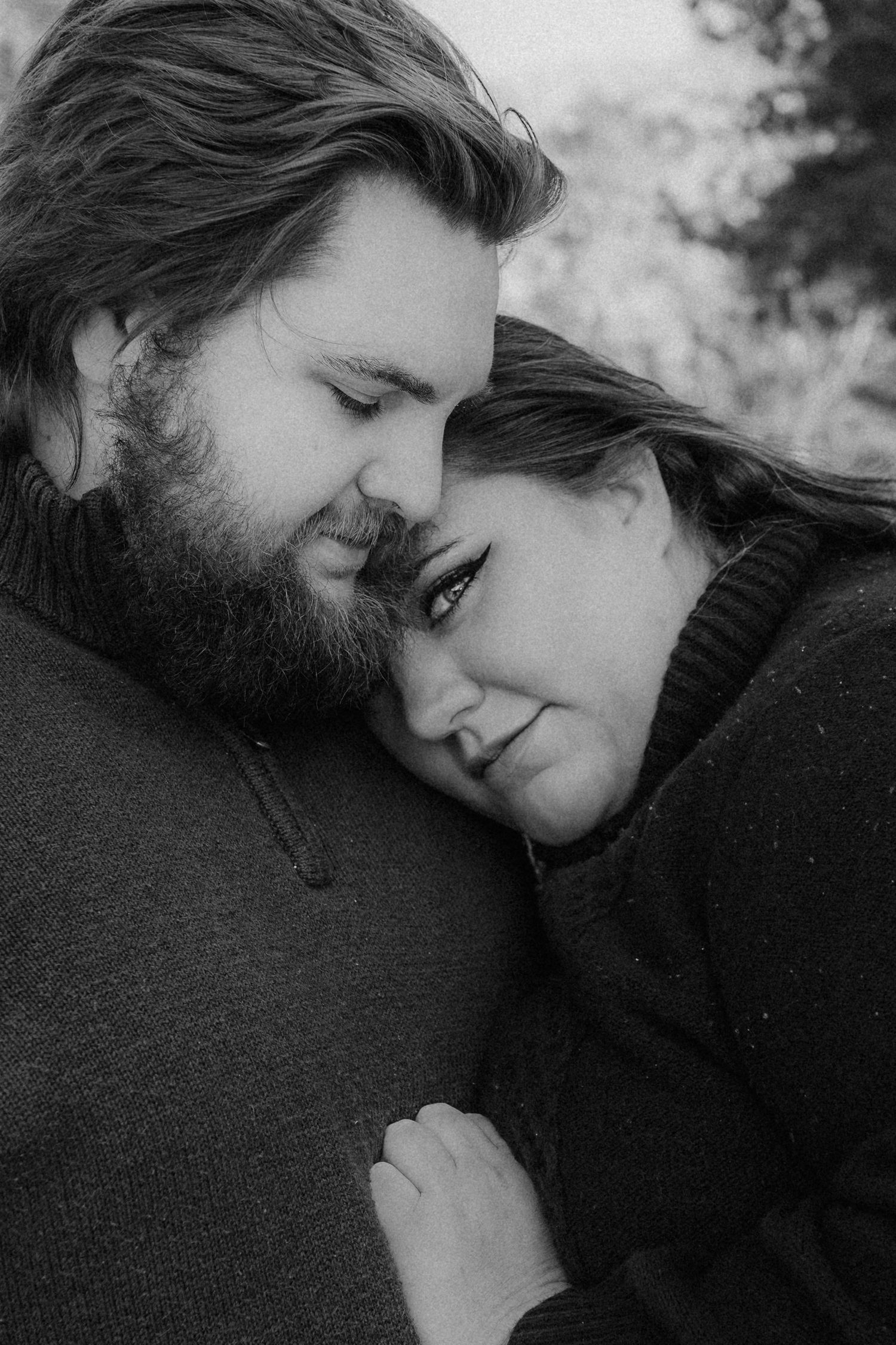 Intimate black and white portrait of couple in dark sweaters sharing tender moment together.