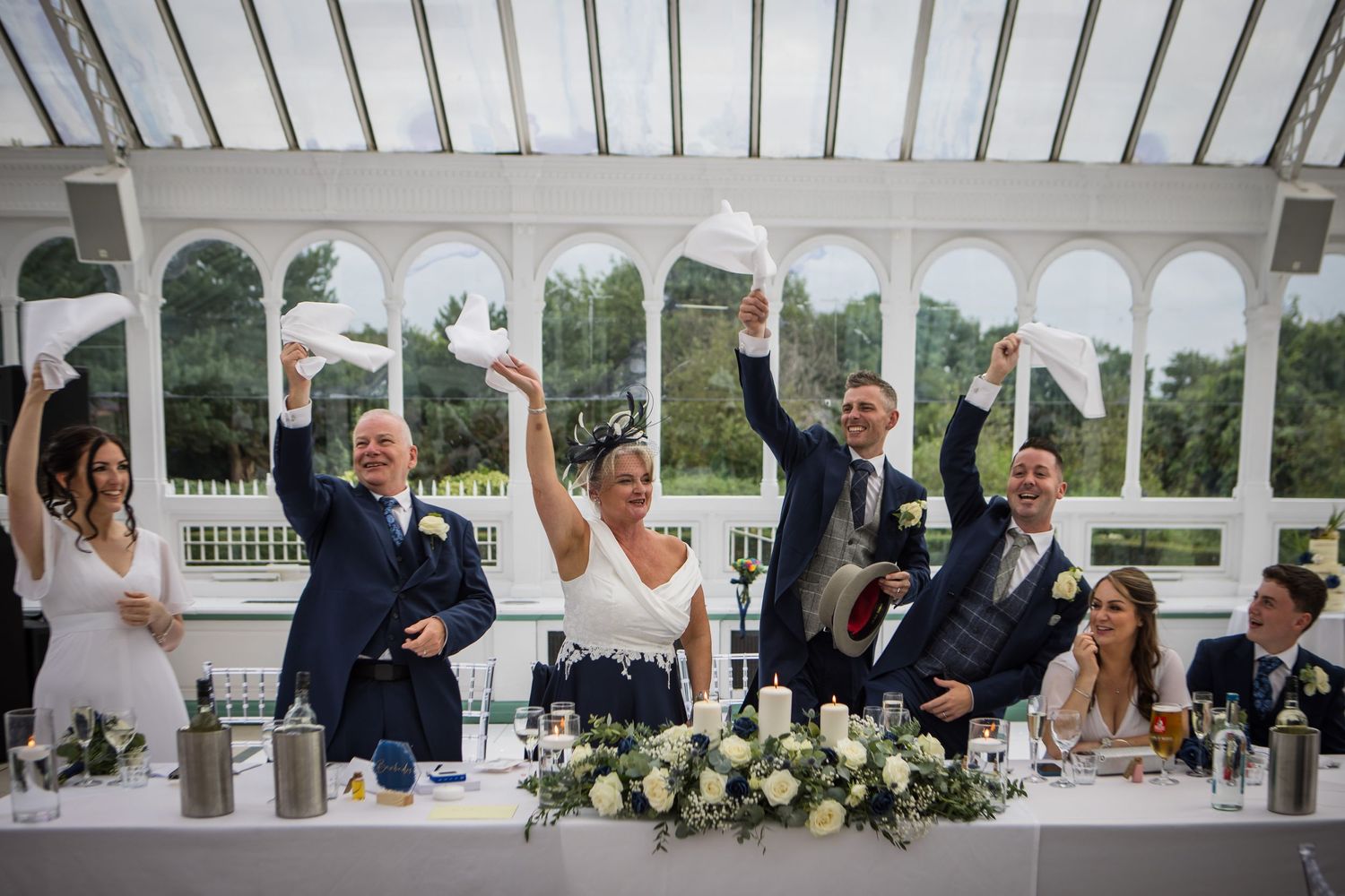 Lively wedding reception scene in white conservatory with guests celebrating.