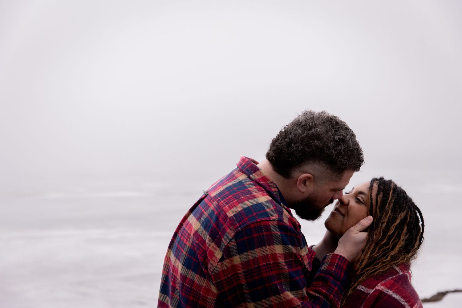 A romantic couple in a plaid shirt shares an intimate moment against a misty gray backdrop.