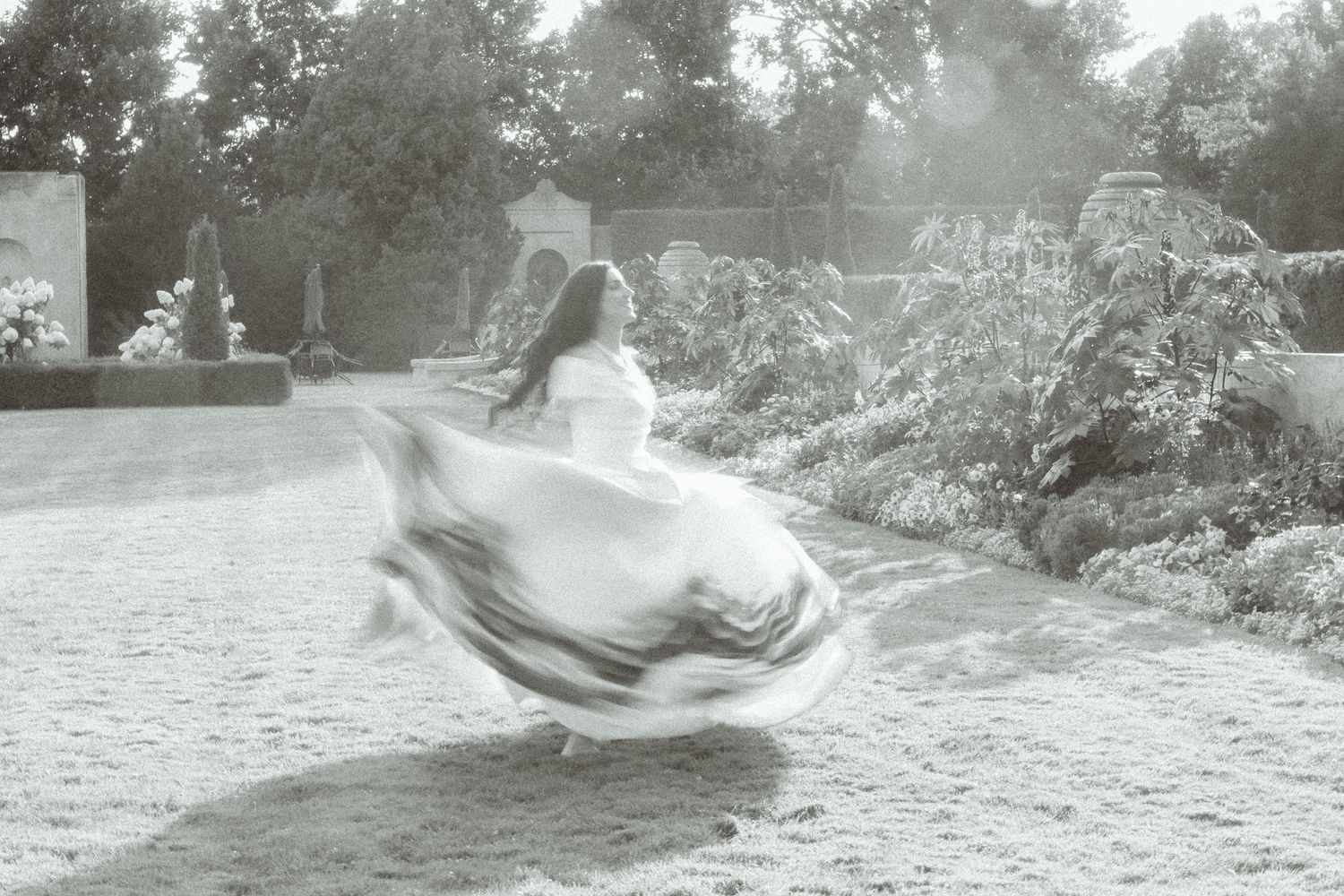 Black and white photo of a whimsical bride twirling in her dress outdoors in a garden setting.