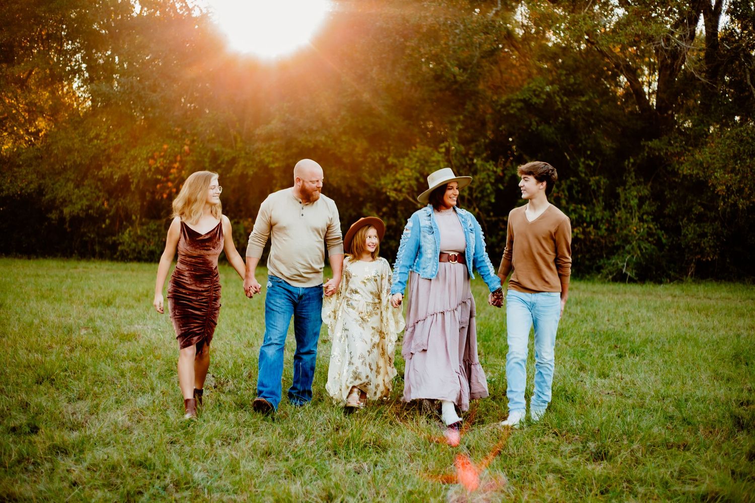 A multi-generational family walks together in a sun-lit field at golden hour.